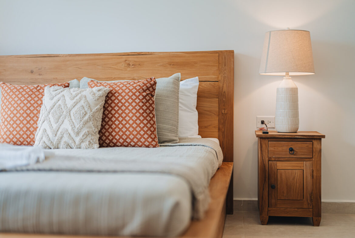 Bedroom detail with wood bed frame, patterned pillows, and nightstand lamp, Seaside Modern Villa, Aruba