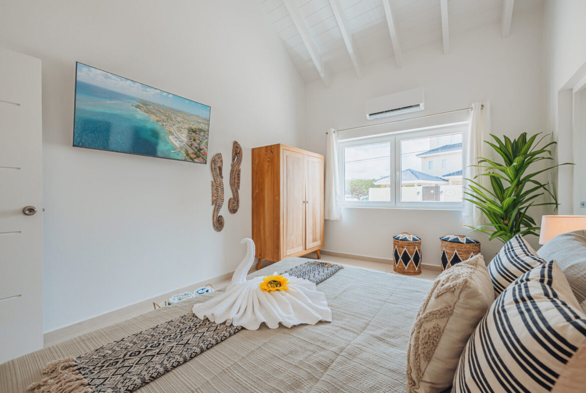 Bedroom with wall-mounted TV, striped throw pillows, and wardrobe, Seaside Modern Villa, Aruba