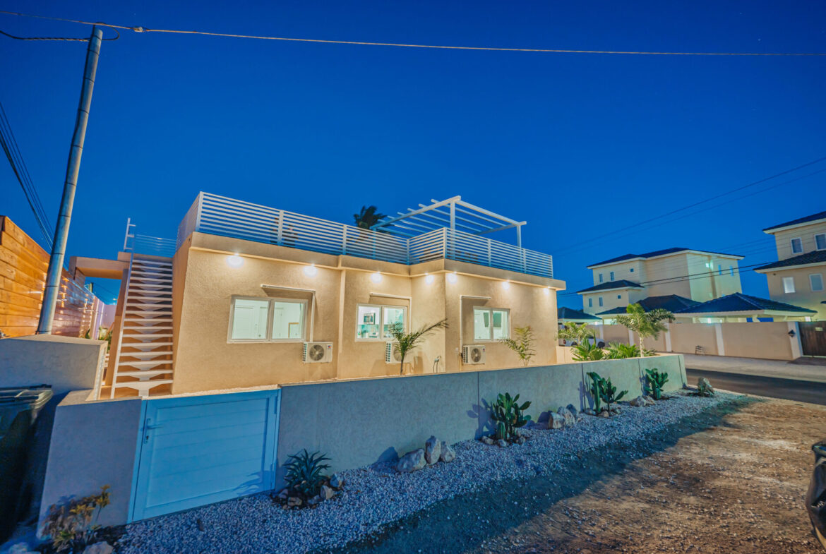 Twilight exterior view of Seaside Modern Villa with illuminated rooftop terrace, Aruba