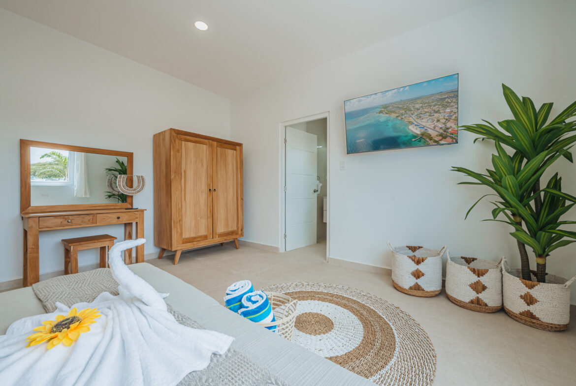Bedroom with vanity desk, wardrobe, wall-mounted TV, and woven rug, Seaside Modern Villa, Aruba