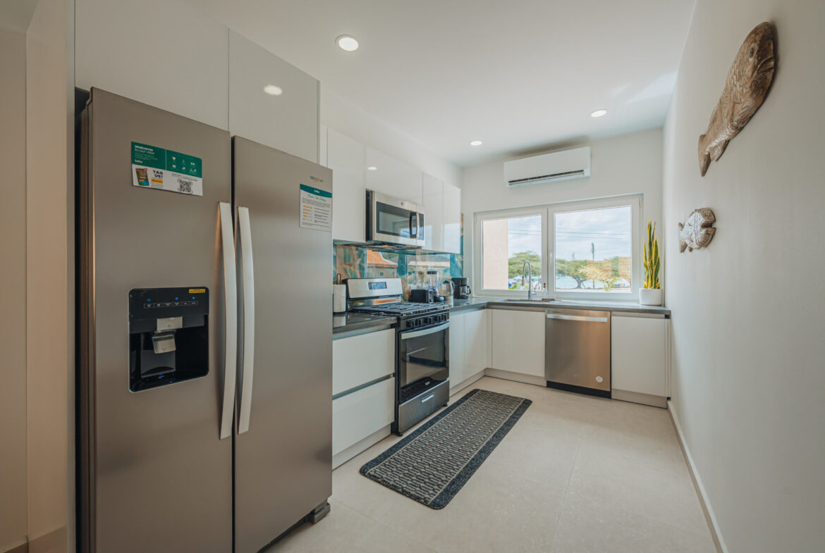 Galley kitchen with stainless refrigerator, dishwasher, and window over the sink, Seaside Modern Villa, Aruba